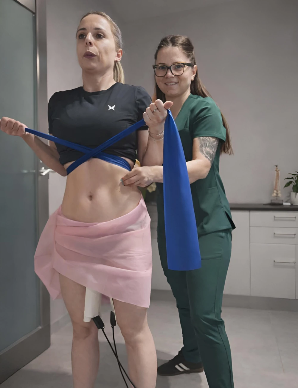 Marzena Sobota, fizjoterapeutka ze Starachowic, stoi w gabinecie w zielonym fartuchu, trzymając pacjentkę za mięśnie brzucha i uśmiechając się do kamery.
